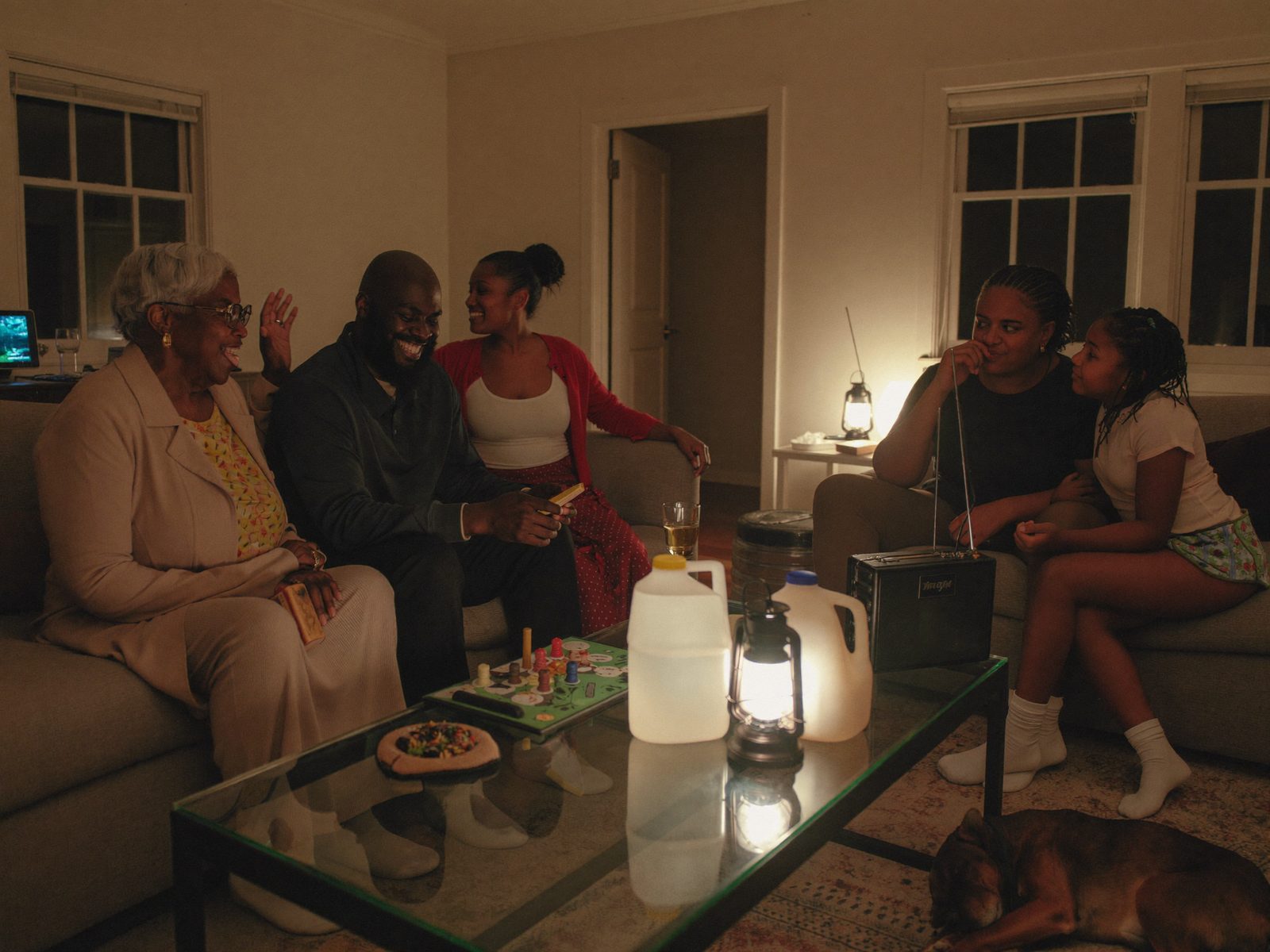 A multigenerational family comfortably operating at home by lantern light — board game, radio, stored water
