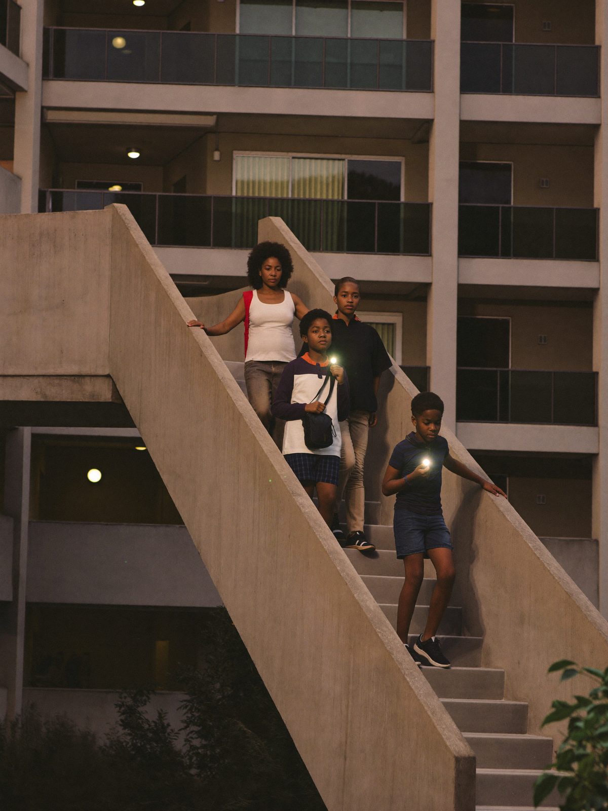 A family walking down a high-rise stairwell in single file with flashlights during an outage